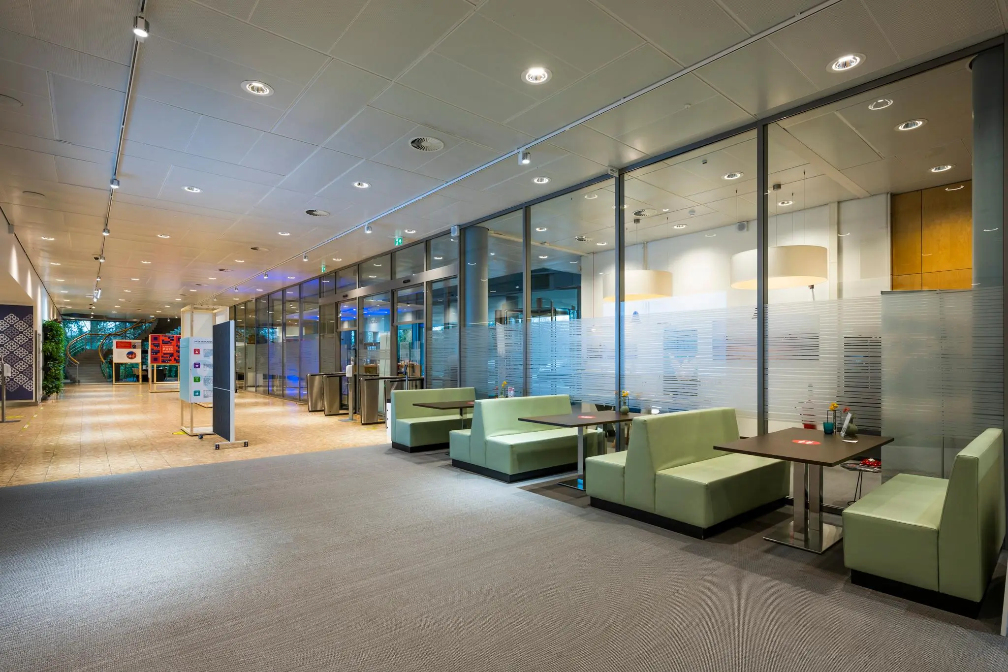 Moderne wachtruimte met groene zitbanken en glazen wanden in een gebouw aan de Burgemeester Rijnderslaan.